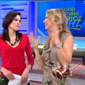 Two women interacting on a television set, one wearing a red top and the other in a beige dress. - Olive Oil Times