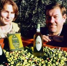 Due individui in posa con bottiglie di olio d'oliva e una cassa di olive in un campo. - Olive Oil Times
