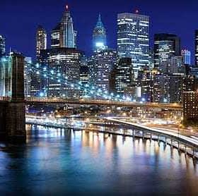 Vue nocturne du pont de Brooklyn avec les toits illuminés de la ville de New York en arrière-plan. - Olive Oil Times