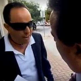 Dos hombres hablando afuera, uno con gafas de sol y traje oscuro, el otro con traje y corbata. - Olive Oil Times