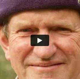 Gros plan d'un homme avec un bonnet violet souriant à la caméra dans un cadre naturel. - Olive Oil Times