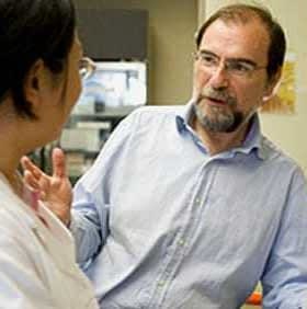 Two individuals, one wearing a white lab coat, engaged in a conversation in a laboratory environment. - Olive Oil Times