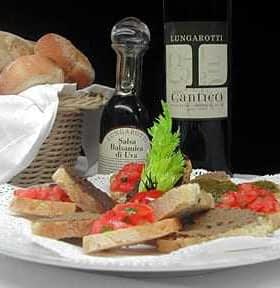 A plate of bruschetta topped with tomatoes and herbs, accompanied by a bottle of olive oil and a basket of bread. - Olive Oil Times