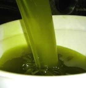 Green olive oil being poured from a container into a white bowl. - Olive Oil Times