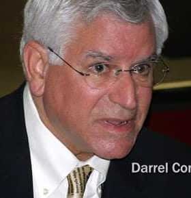 Darrel Corti engaged in conversation during a public event, wearing glasses and a suit. - Olive Oil Times