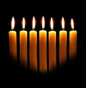 Eight yellow candles arranged in a row, each with a flame, against a dark background. - Olive Oil Times