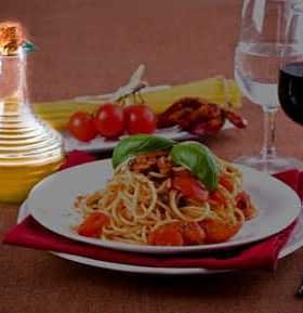 A plate of spaghetti topped with tomatoes and basil, accompanied by a cruet of olive oil and glasses of water and red wine. - Olive Oil Times