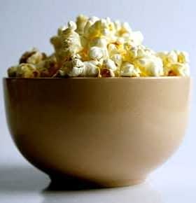A beige bowl filled with freshly popped popcorn against a plain background. - Olive Oil Times