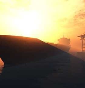 Silhouette of a large ship against a sunset backdrop with cranes in the background. - Olive Oil Times
