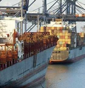 Two cargo ships docked at a port with containers stacked on their decks. - Olive Oil Times