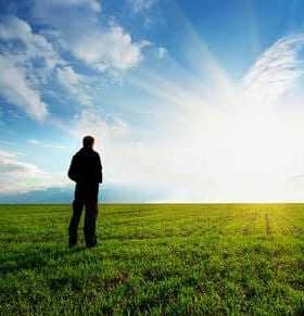 Silhouette of a person standing on a green field with a blue sky and clouds in the background. - Olive Oil Times