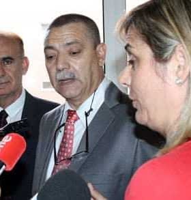 Three individuals, two men and one woman, engaged in a discussion with microphones present. - Olive Oil Times