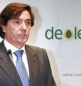 Man in a suit speaking at a presentation with Deoleo logo in the background. - Olive Oil Times