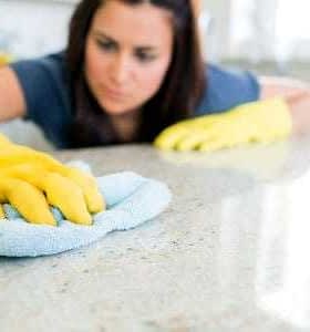 Individual wearing yellow gloves cleaning a countertop with a blue cloth in a bright indoor setting. - Olive Oil Times