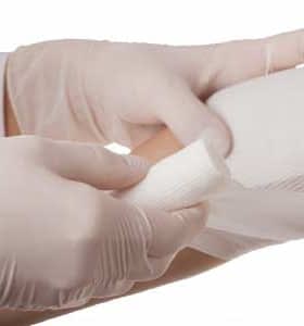 A medical professional in gloves applying a bandage to a patient's arm. - Olive Oil Times