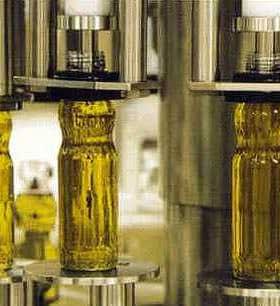 Three glass bottles filled with olive oil being processed on a bottling line. - Olive Oil Times