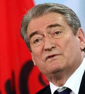 Man speaking at a podium with an Albanian flag in the background. - Olive Oil Times