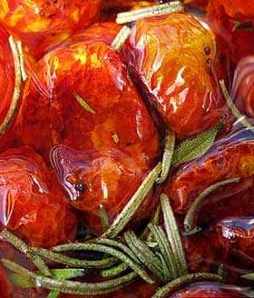 Close-up of oven dried tomatoes submerged in olive oil with rosemary sprigs. - Olive Oil Times