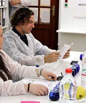 A group of individuals in lab coats engaged in a discussion around a table with various items and documents. - Olive Oil Times