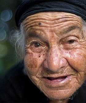 Close-up portrait of an elderly woman wearing a black headscarf and smiling at the camera. - Olive Oil Times