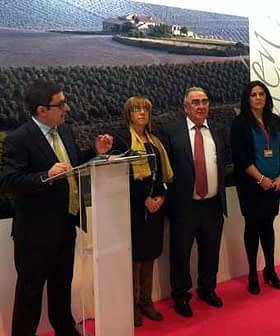 Four individuals standing at a podium during a presentation at an event, with a backdrop of olive fields. - Olive Oil Times