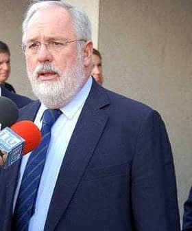 Three men at a press conference, one speaking into microphones while the others listen attentively. - Olive Oil Times