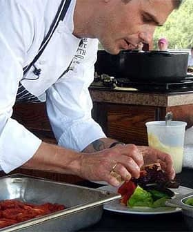 Chef in a white coat arranging salad ingredients on a plate during a cooking demonstration. - Olive Oil Times