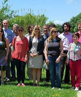 A group of diverse individuals posing together outdoors in a green area with trees and grass. - Olive Oil Times