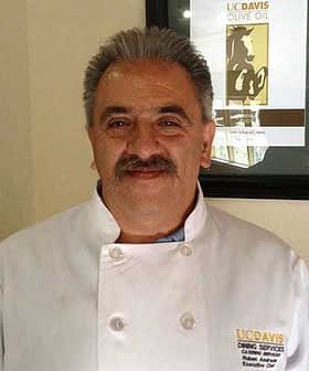 A chef wearing a white coat with a UC Davis logo, smiling in a well-lit indoor setting. - Olive Oil Times