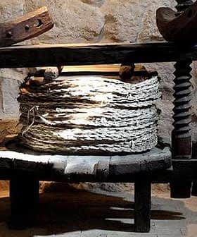 An ancient olive oil press made of wood with a circular base and a large cylindrical container. - Olive Oil Times