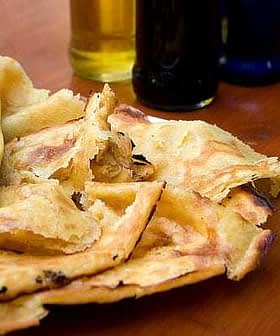 A plate of socca, a type of flatbread, with several bottles of olive oil in the background. - Olive Oil Times