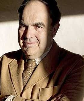 A man wearing a brown suit with arms crossed, sitting in a well-lit area with shadows. - Olive Oil Times