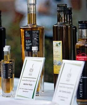Assorted bottles of olive oil with labels displayed on a table at an event. - Olive Oil Times