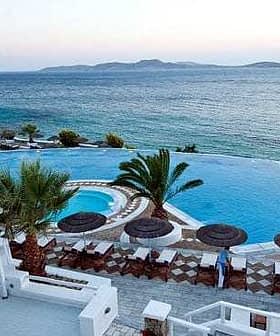 Infinity pool with palm trees and lounge chairs beside the sea at a resort. - Olive Oil Times