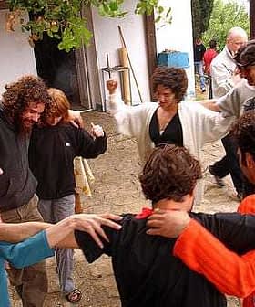 A group of people dancing in a circle, with some wearing colorful clothing and showing joyful expressions. - Olive Oil Times