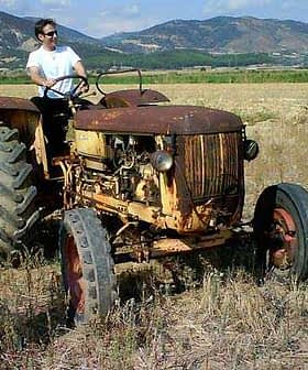 A vintage tractor in a field with two men standing nearby, one taking a photo. - Olive Oil Times