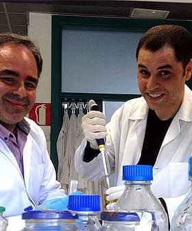 Two male scientists wearing lab coats and gloves working with laboratory equipment and bottles. - Olive Oil Times
