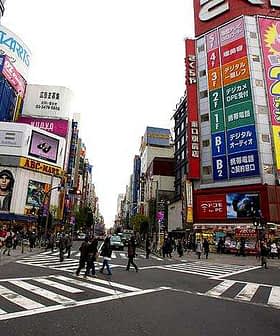 A busy intersection in Tokyo featuring large advertisements and pedestrians crossing the street. - Olive Oil Times