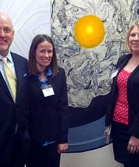 Five individuals standing together in front of a large circular artwork featuring a yellow center. - Olive Oil Times