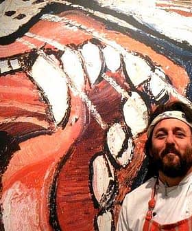 Chef with a beard and white chef's coat standing beside a large colorful mural of a lion's face. - Olive Oil Times