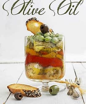 Book cover for 'Cooking Techniques with Olive Oil' featuring a glass container with layered ingredients and herbs. - Olive Oil Times