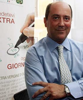 A businessman in a blue dress shirt standing with arms crossed in an office environment. - Olive Oil Times