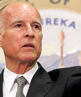 Man in a gray suit pointing while speaking at a podium with a seal in the background. - Olive Oil Times