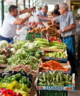 Vendors and customers interacting at a fresh produce market with various vegetables displayed. - Olive Oil Times