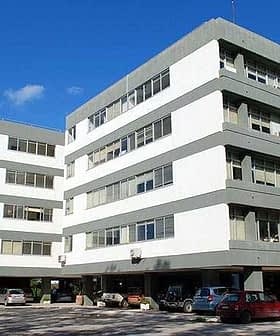 A multi-story office building featuring a modern architectural design with large windows and a gray and white color scheme. - Olive Oil Times