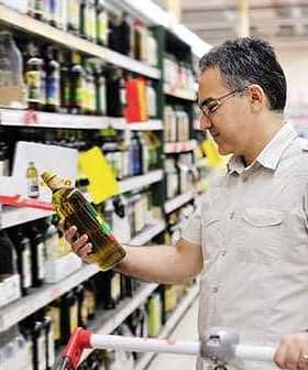 Man holding a bottle of olive oil while shopping in a grocery store aisle. - Olive Oil Times