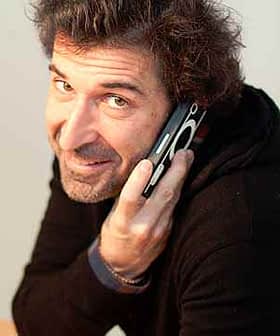 Man with curly hair holding a mobile phone to his ear while smiling. - Olive Oil Times