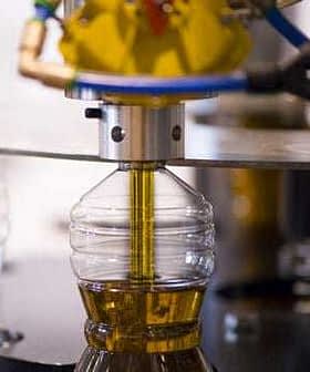 Machine filling a plastic bottle with olive oil during the bottling process. - Olive Oil Times