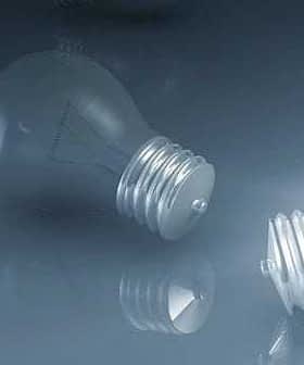 A light bulb with a metallic base and a reflective surface lying on a smooth surface. - Olive Oil Times