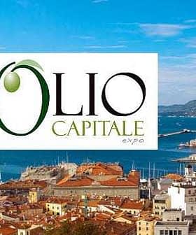 Logo of Olio Capitale Expo displayed over a coastal city view with boats and buildings. - Olive Oil Times